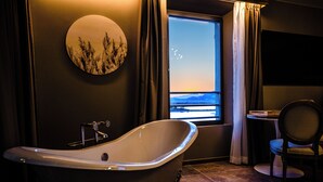 A bathroom with a freestanding bathtub, a round wall decoration, a window with a view, and a chair. - Le Hameau des Pesquiers Ecolodge, Curio Collection by Hilton (Hyères)