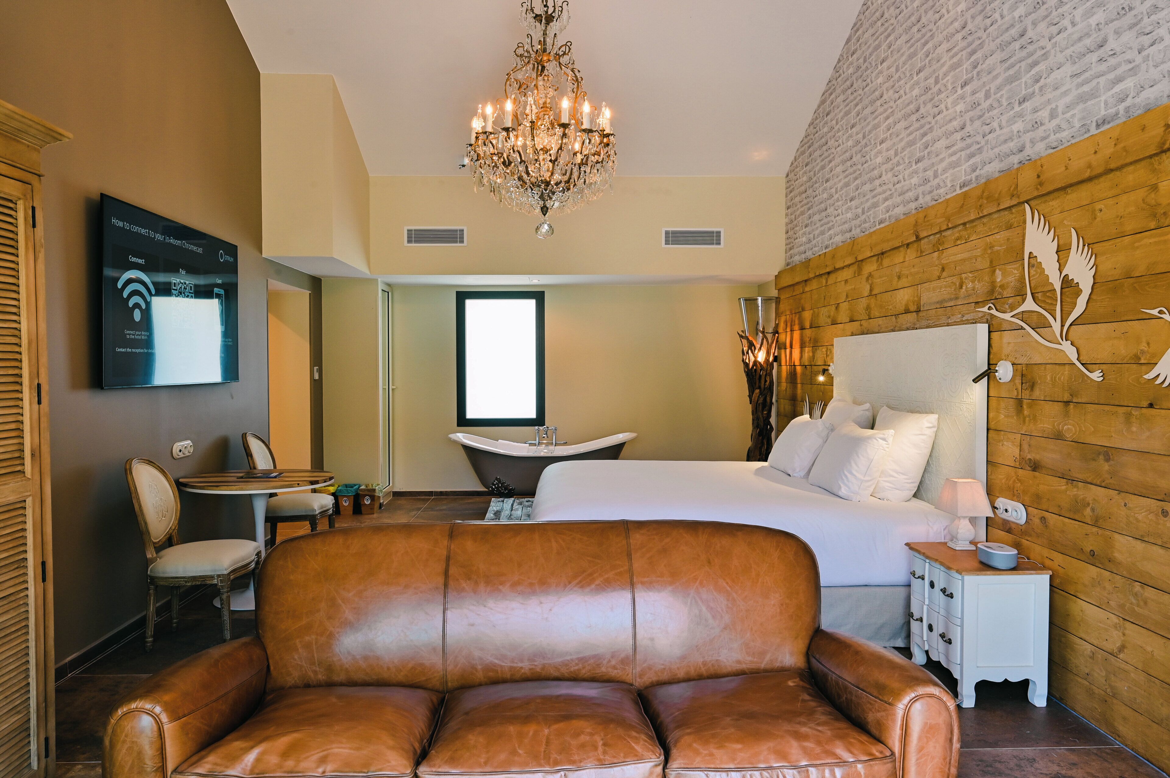 Un dormitorio con una cama grande, un candelabro, una pared de madera, una mesita de noche blanca y un televisor que muestra una guía de conexión Wi-Fi.