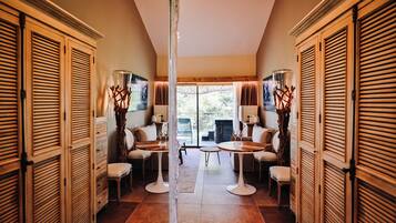 A hallway with wooden shutters, two round tables with chairs, and a view to the outside.