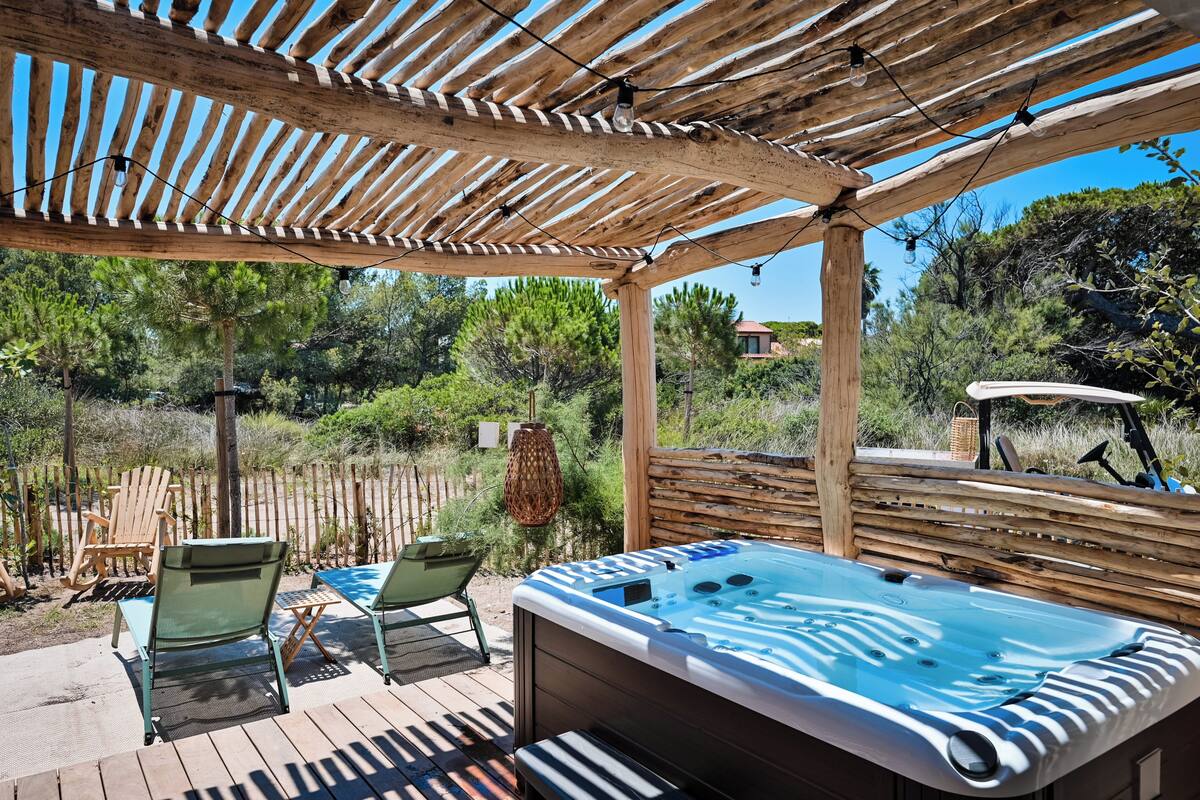 A wooden deck with a hot tub, lounge chairs, and a pergola.