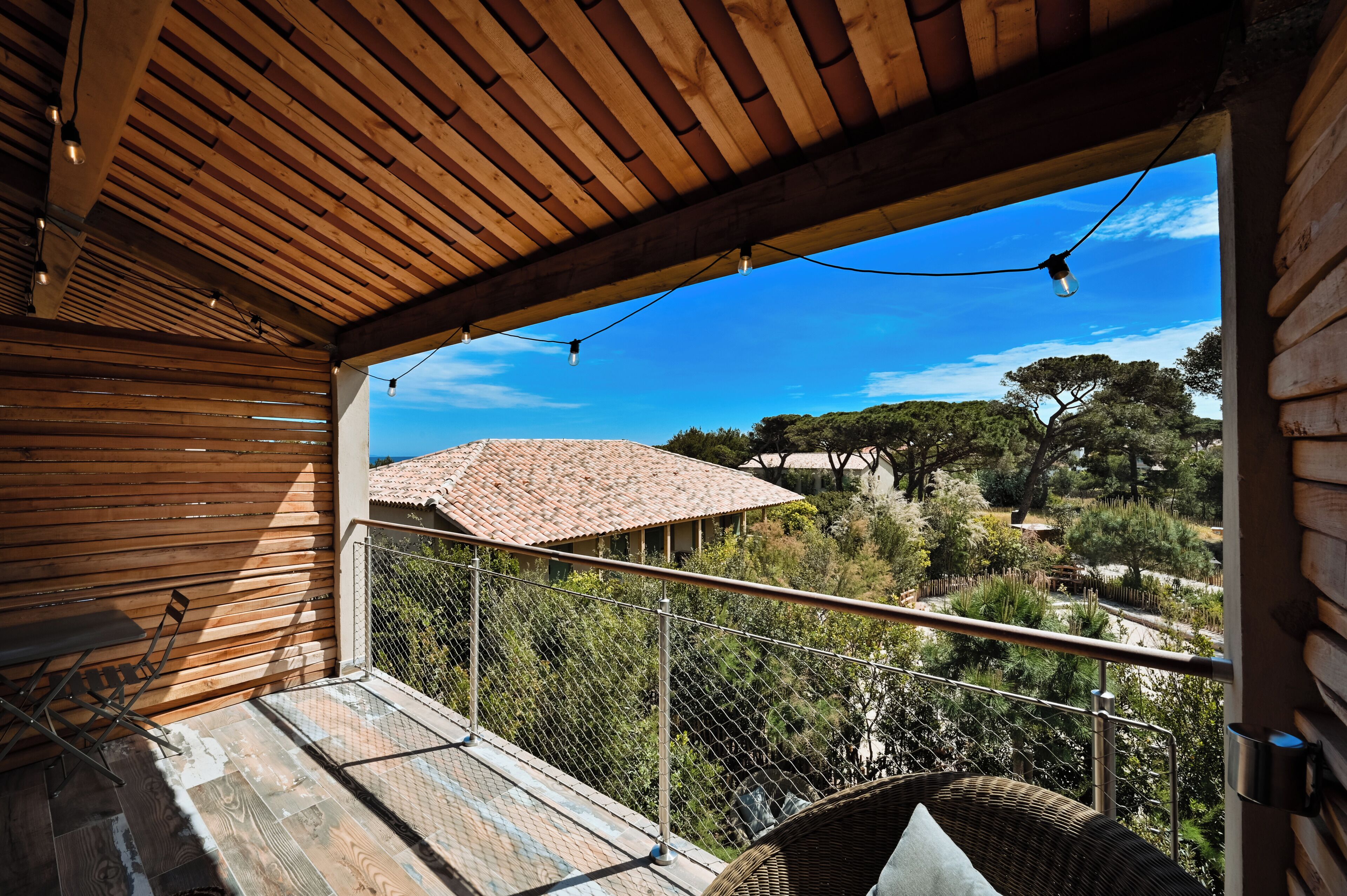 A wooden balcony with a view of a rural landscape, a metal railing, and a wicker chair.