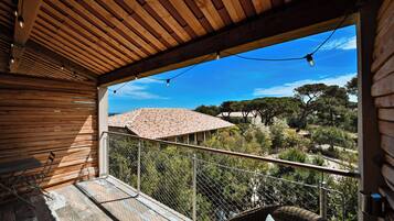 A wooden balcony with a view of a rural landscape, a metal railing, and a wicker chair.
