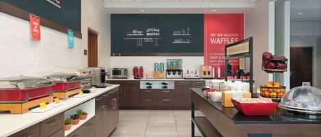 A modern kitchen area with a buffet setup, including a variety of food items and a chalkboard with writing.