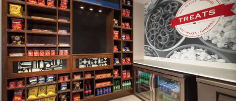 A snack display with various chips and snacks, a refrigerated section with beverages, and a wall with a 'Treats' sign.