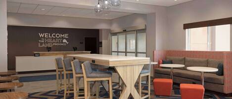 A modern hotel lobby with a reception desk, bar stools, a sofa, and a patterned carpet.