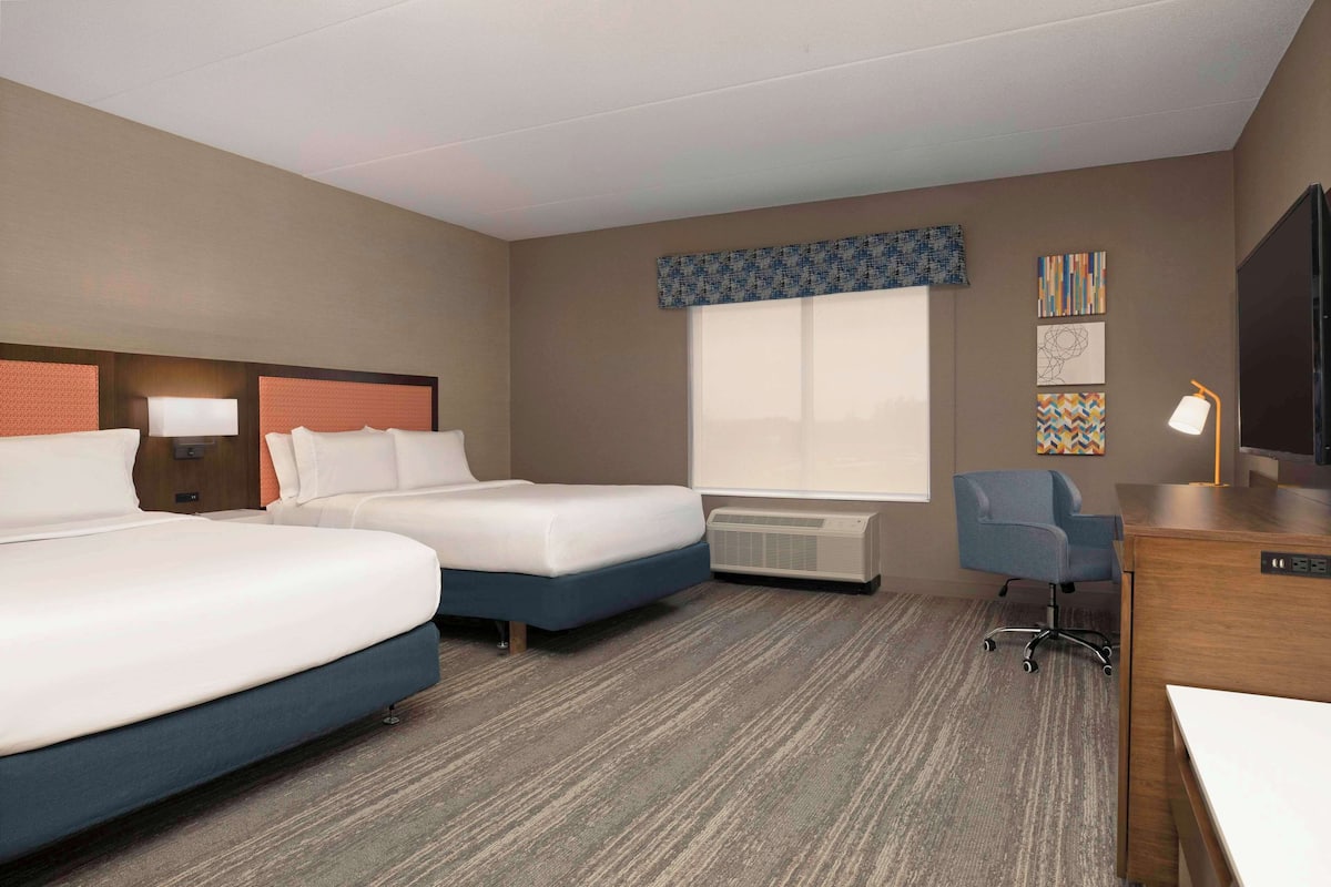 A hotel room with two beds, a desk, a chair, a TV, and a window with a view.