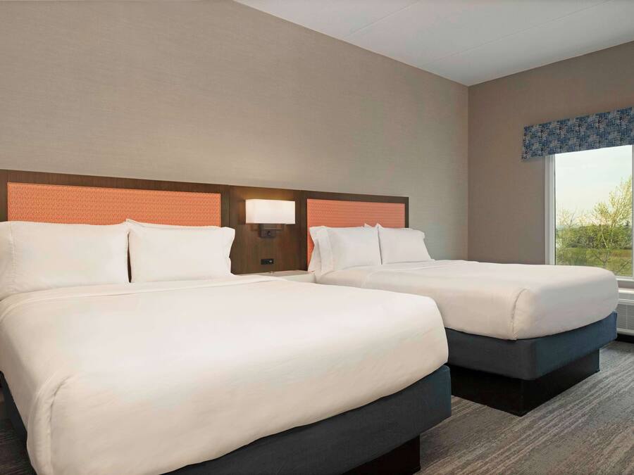Hotelkamer met twee bedden, een nachtkastje met een lamp en een groot raam met uitzicht op groen.