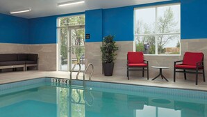 An indoor swimming pool with clear water, a blue and white wall, a potted plant, and red chairs. - Hampton Inn by Hilton Port Hope Cobourg (Port Hope)