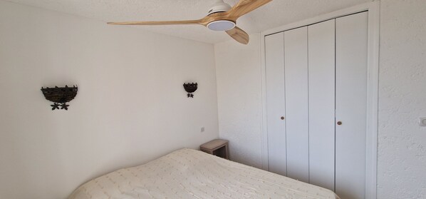 A bedroom with a bed, a ceiling fan, a wardrobe, and wall-mounted decorations.