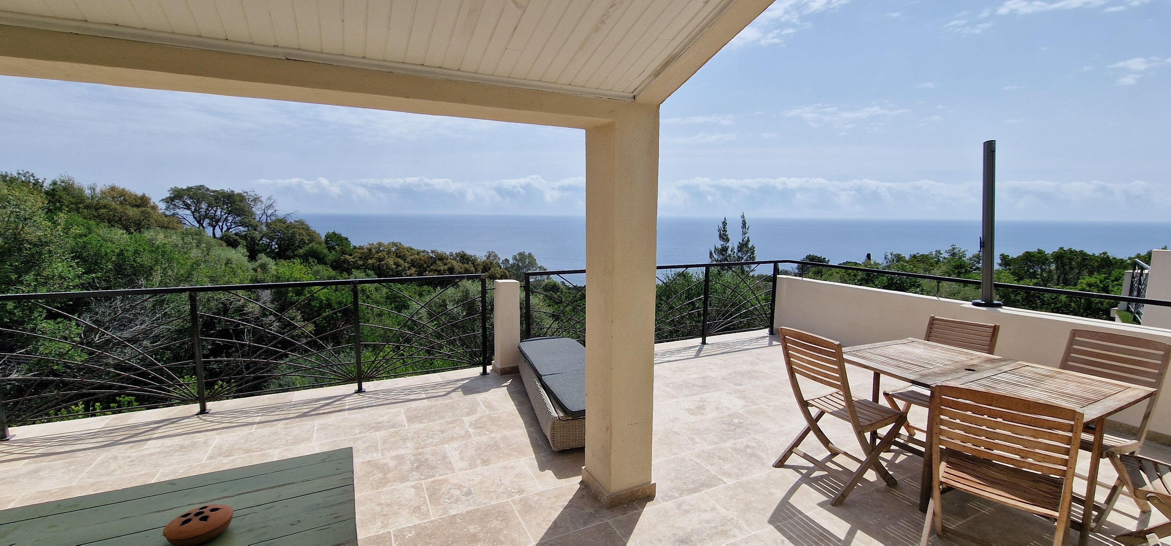 Un balcón con vista al mar, mobiliario exterior y una estructura de pérgola.