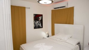 Een netjes opgemaakt bed met witte lakens, een bedlampje en een ingelijste foto aan de muur.