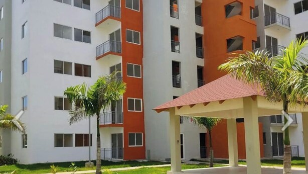 Een modern appartementencomplex met meerdere gebouwen, buitenpaden en kleine palmboompjes.