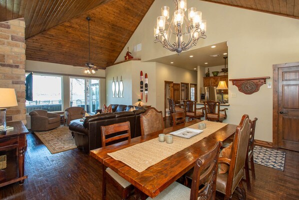 A spacious dining area with a wooden table and chairs, a chandelier, and a view of the kitchen and living room.