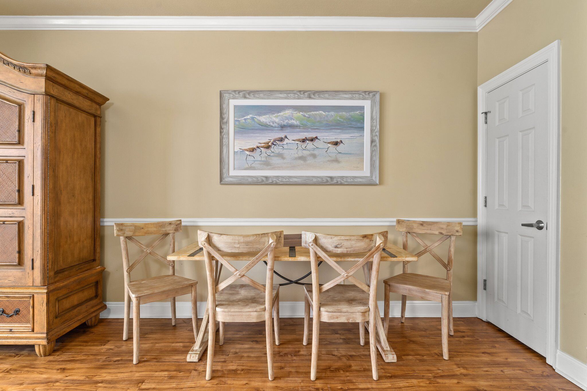 Un comedor con una mesa y sillas de madera, un cuadro de pájaros en la pared y un armario de madera.