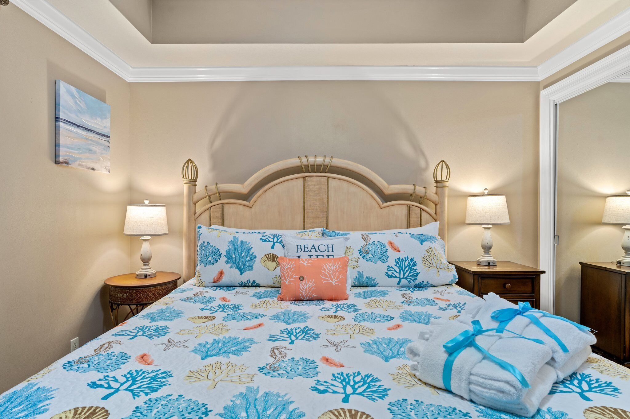 A bedroom with a bed featuring a beach-themed bedspread, two bedside lamps, and a nightstand with a lamp.