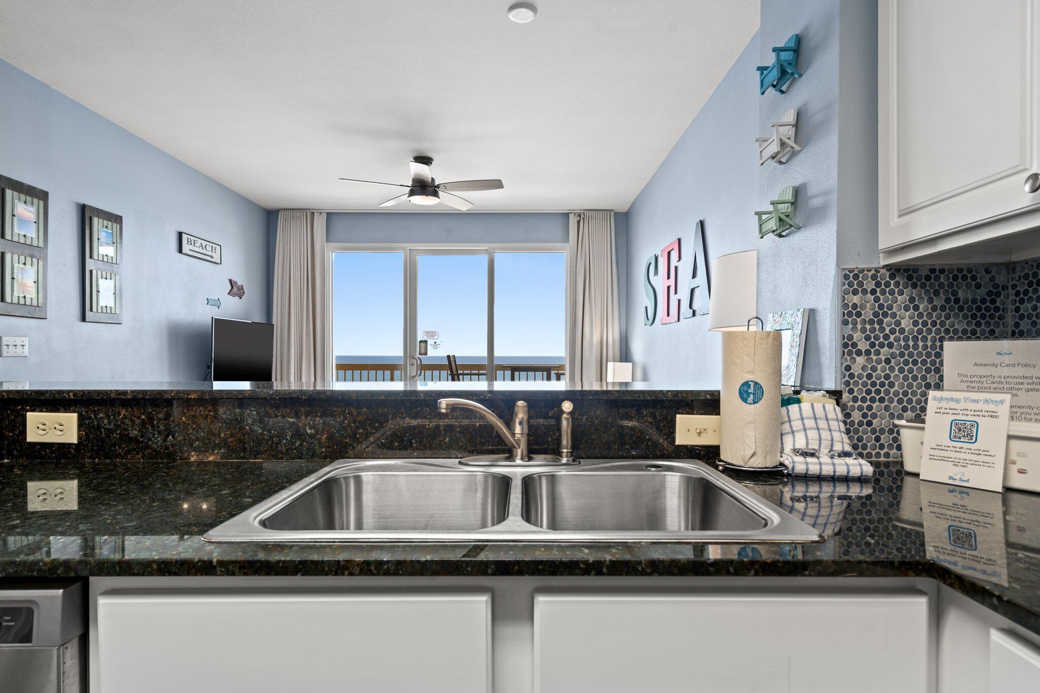A modern kitchen with a large window, a ceiling fan, and a view of the beach.
