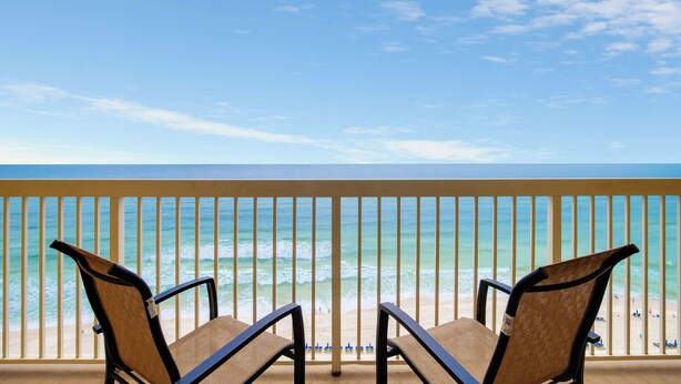 A balcony with two chairs facing a beach with waves and a clear sky. - Calypso By Blue Swell (Panama City Beach)