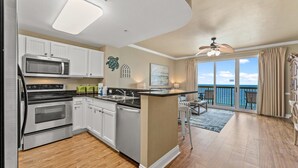 A modern kitchen with white cabinets, stainless steel appliances, and a large island. There is a balcony with a view of the ocean. - Calypso By Blue Swell (Panama City Beach)