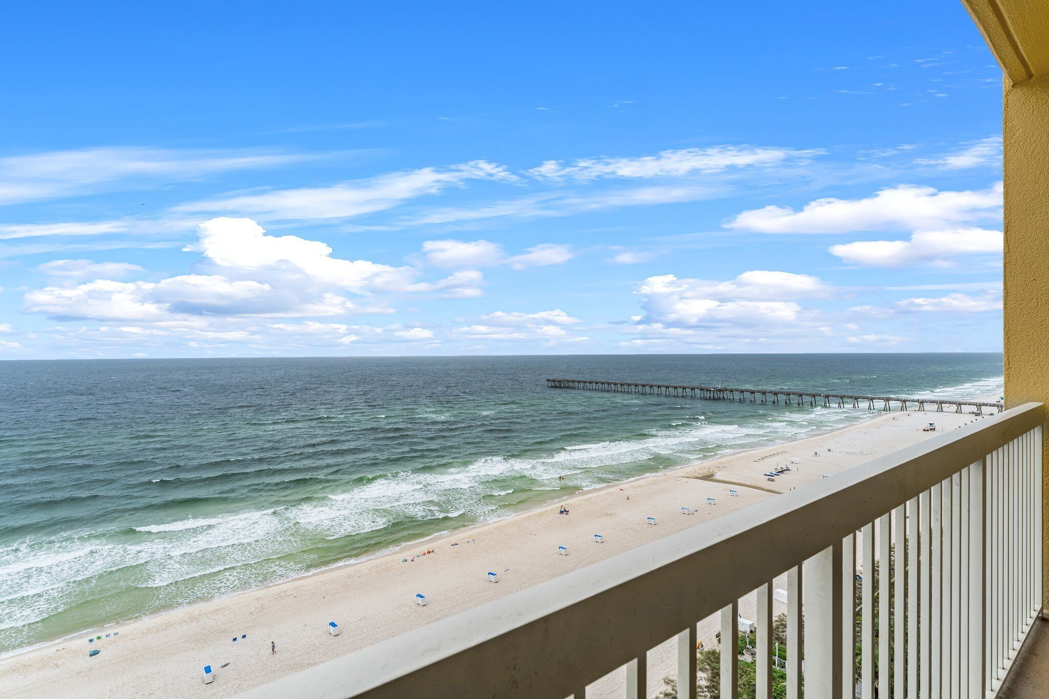 A beach with a pier extending into the ocean, a sandy shore with beach umbrellas, and a clear sky.