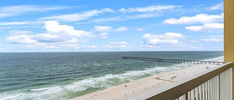 A beach with a pier extending into the ocean, a sandy shore with beach umbrellas, and a clear sky.
