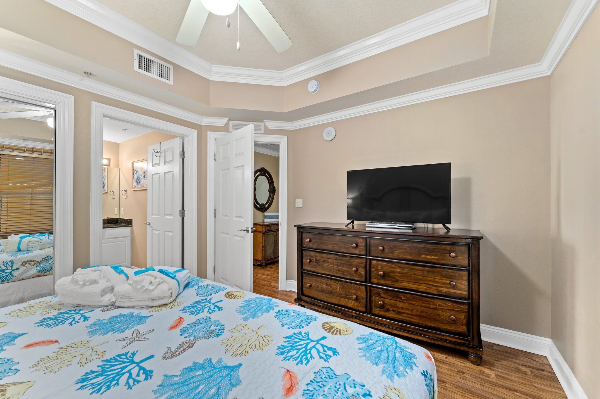 A bedroom with a bed, a dresser, a television, and a bathroom visible through an open door.