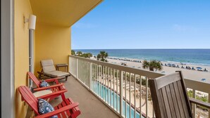 A balcony with red chairs, a small table, and a view of the beach and ocean. - Calypso By Blue Swell (Panama City Beach)