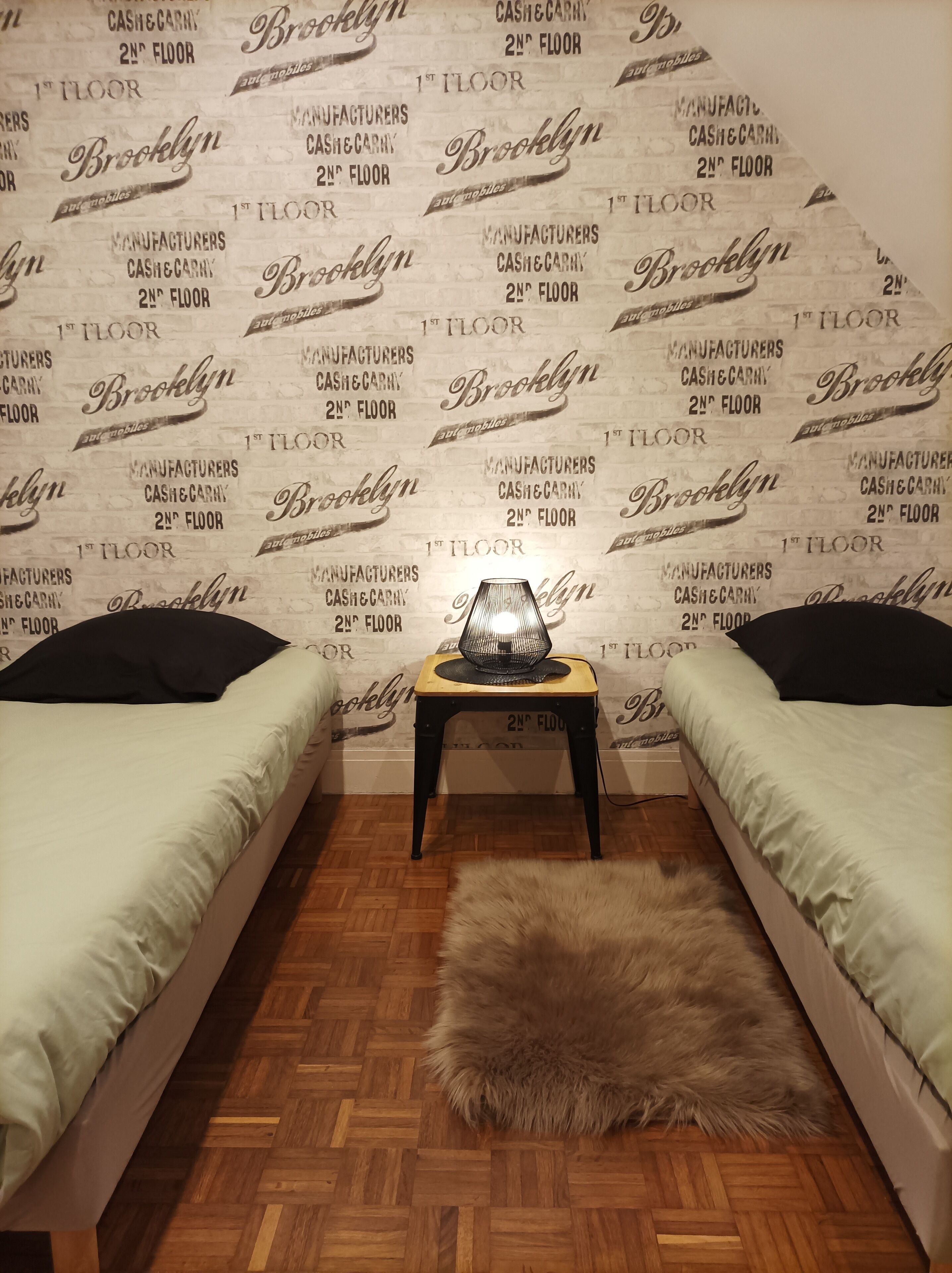 Ein Schlafzimmer mit zwei Betten, einem kleinen Tisch mit Lampe und einem flauschigen Teppich auf Holzboden.