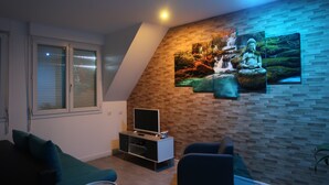 Een woonkamer met een televisie, een bank, een salontafel en een aan de muur bevestigde televisie waarop natuurscènes worden getoond.
