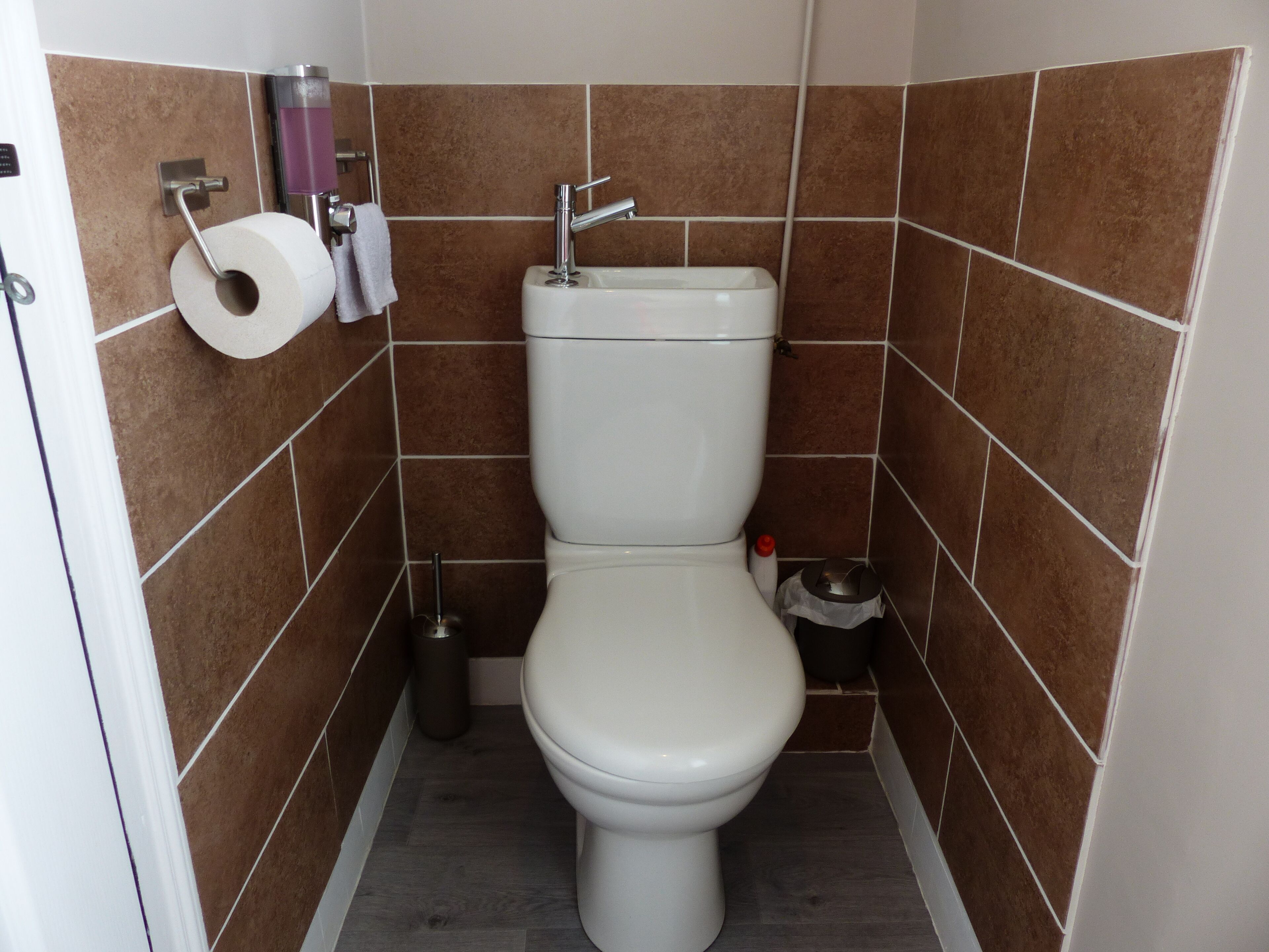 A small bathroom with a toilet, a sink, and a trash bin.