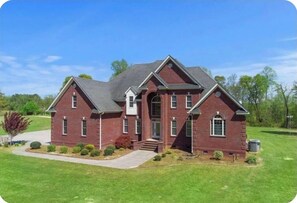 A two-story brick house with a gabled roof, a front porch, and a well-maintained lawn.