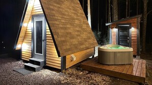 Una cabana de fusta triangular amb un bany d'hidromassatge i una construcció de fusta a part.