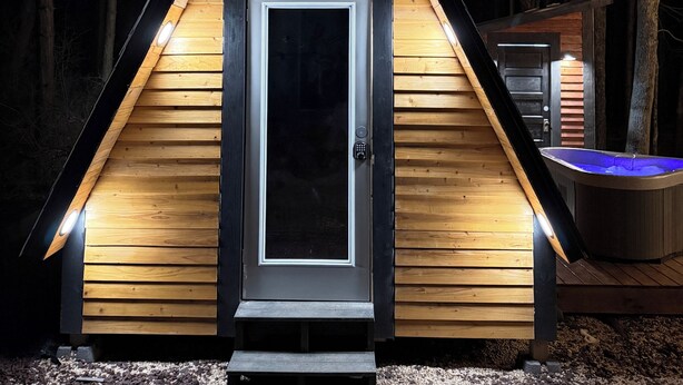 Una petita cabana de fusta triangular amb una porta fosca, il·luminada per llums a l'entrada.