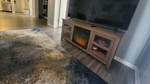 Una sala de estar con un televisor de pantalla plana sobre un soporte de madera, una chimenea y una alfombra estampada.