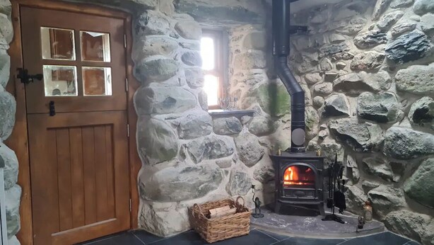 Ein Zimmer mit Steinwänden, einer Holztür, einem Kamin und einem Fliesenboden.