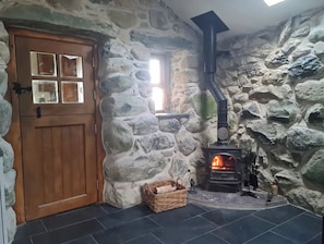 Une pièce aux murs de pierre, dotée d’une porte en bois, d’une cheminée et d’un sol carrelé.