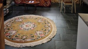 Ein gemütliches Zimmer mit Steinwand, Holzbalkendecke, einer Couch, einem Esstisch und einem Teppich.