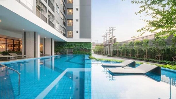 A modern hotel with a large indoor swimming pool, lounge chairs, and a well-maintained garden area. - Lovely 2-bed Apart - 19th Floor Notting Hill Bldg (Samut Prakan)