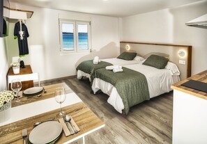 A hotel room with two beds, a wooden dining table, and a view of the sea through a window.