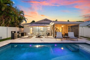 A backyard with a swimming pool, outdoor furniture, and a covered patio area.