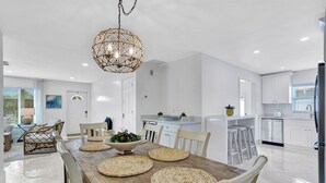 Een moderne keuken met witte kasten, een houten eettafel met geweven placemats en een hanglamp.