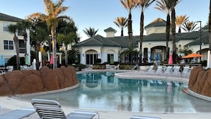 A pool area with lounge chairs, palm trees, and a building with a tiled roof. - Lovely Condo Stay Disney Orlando, 2Bed/2Bath (Kissimmee)