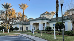 A building with a light-colored facade, a green roof, and a parking lot with marked spaces. - Lovely Condo Stay Disney Orlando, 2Bed/2Bath (Kissimmee)