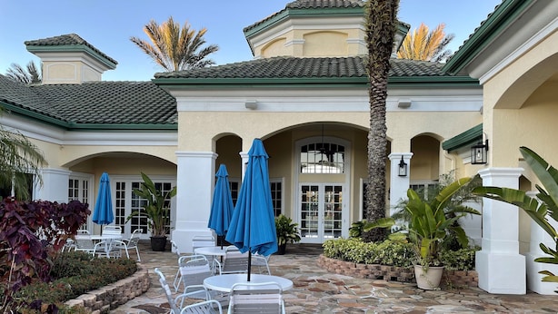 A courtyard with stone flooring, white chairs, blue umbrellas, and potted plants. - Lovely Condo Stay Disney Orlando, 2Bed/2Bath (Kissimmee)