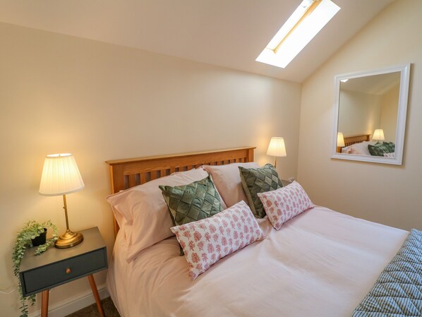 A neatly made bed with a wooden headboard, two bedside lamps, and a mirror on the wall. - The Stable (Lincoln)