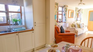 A kitchen with a sink, a dining table with chairs, a sofa, and a window with curtains.