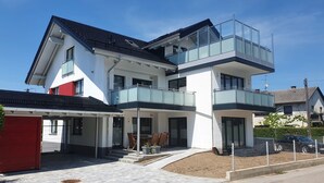 Una casa moderna a due piani con un balcone, un portico coperto e una strada privata.