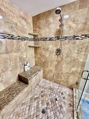 Un baño con ducha, paredes de azulejos, un lavabo con encimera de mármol y desagüe.