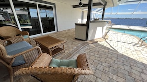 A covered outdoor area with wicker furniture, a pool, and a view of the sea. - Stunning open water view 3 bedroom house, pool, private dock (Cape Coral)