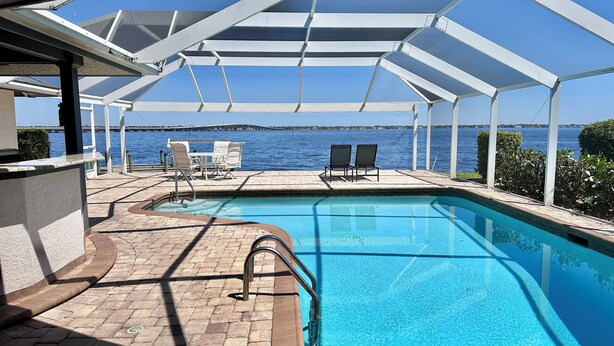 A pool area with a view of the sea, a covered seating area, and a poolside bar. - Stunning open water view 3 bedroom house, pool, private dock (Cape Coral)