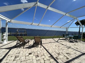 Un patio exterior con vista al mar, que cuenta con una zona de estar cubierta con sillas y una mesa.